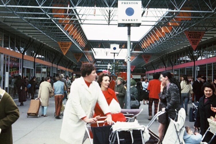 Crowds of people walk back and forth under the metal arches of Preston Market in a photo that appears to be from the 70s or 80s.