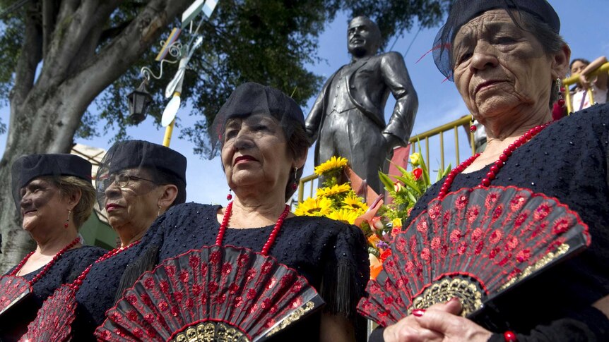 Gardel widows stand next to a statue of Carlos Gardel.