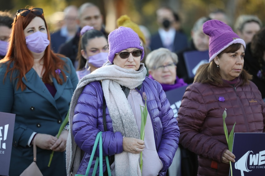 Several women stand wearing purple on a cold day on the lawns of Parliament House.