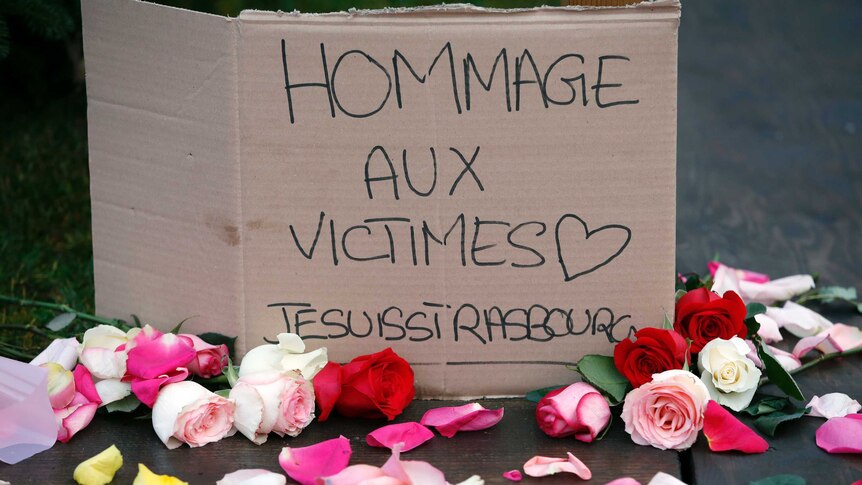 A placard surrounded by roses  reads "Tribute to the victims. I am Strasbourg"