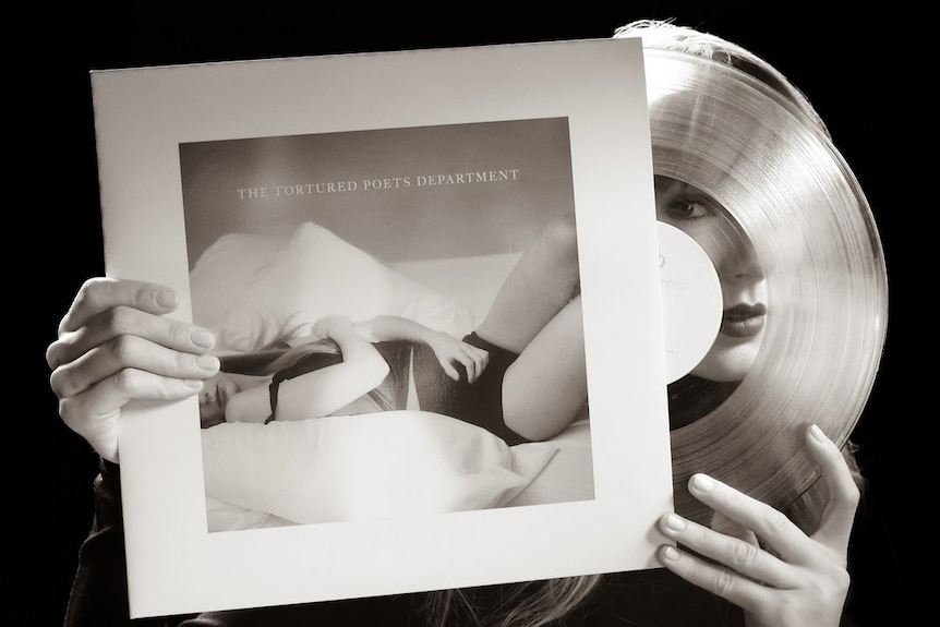 A black and white photo of Swift holding up the album cover, and peering through the transparent vinyl