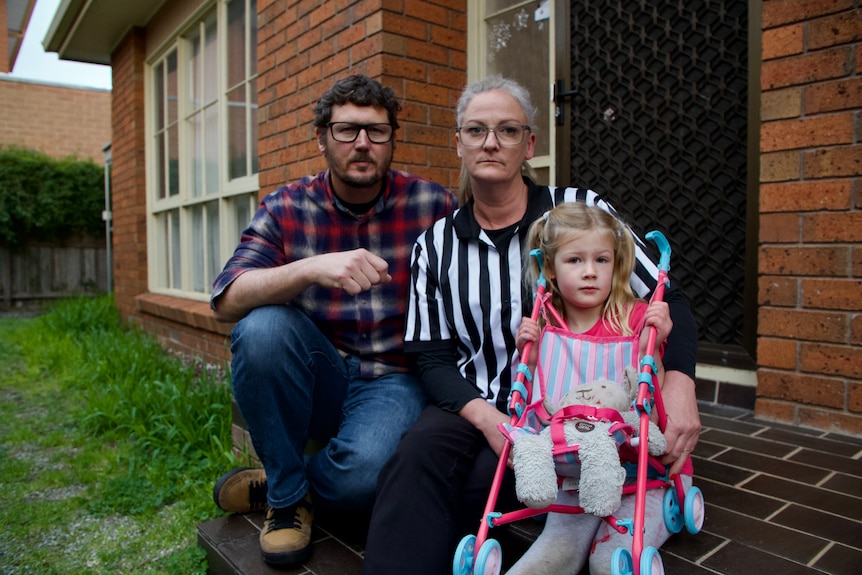 A man, woman and child sit outside on the steps of a house.