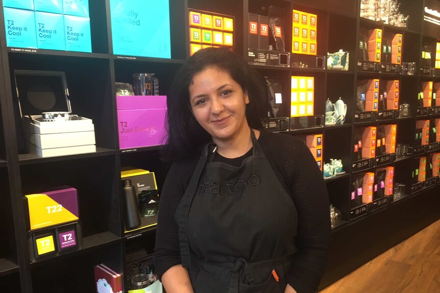 Woman in shop assistant's apron stands in front of different varieties of tea.