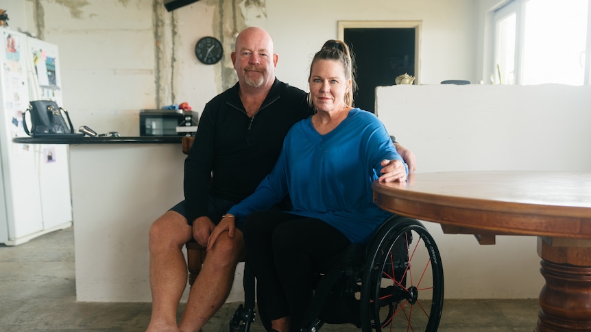 A middle aged couple sit together in their kitchen they are currently renovating.