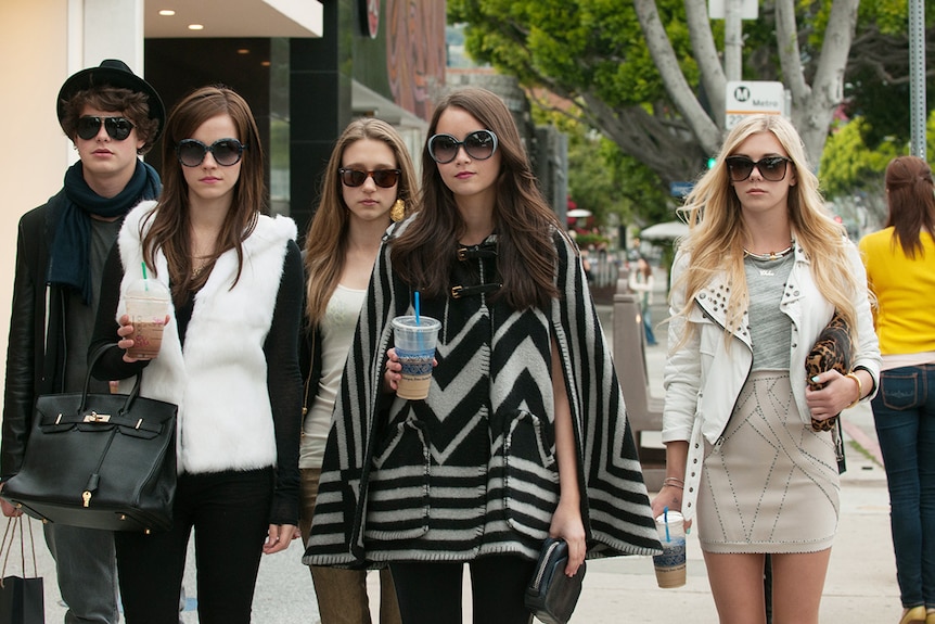 A group of four young white women and a man with big sunglasses and handbags and starbucks coffees in The Bling Ring