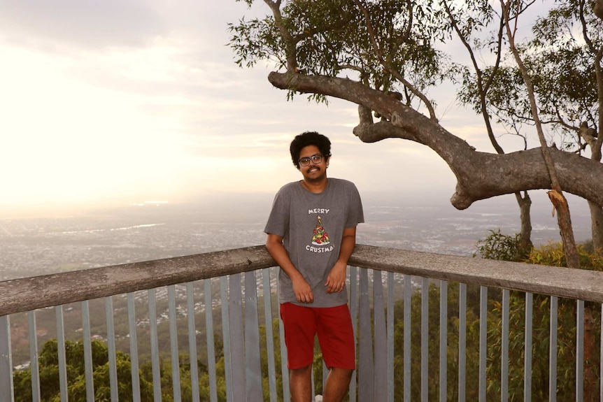 Man stands at lookout with view behind him.