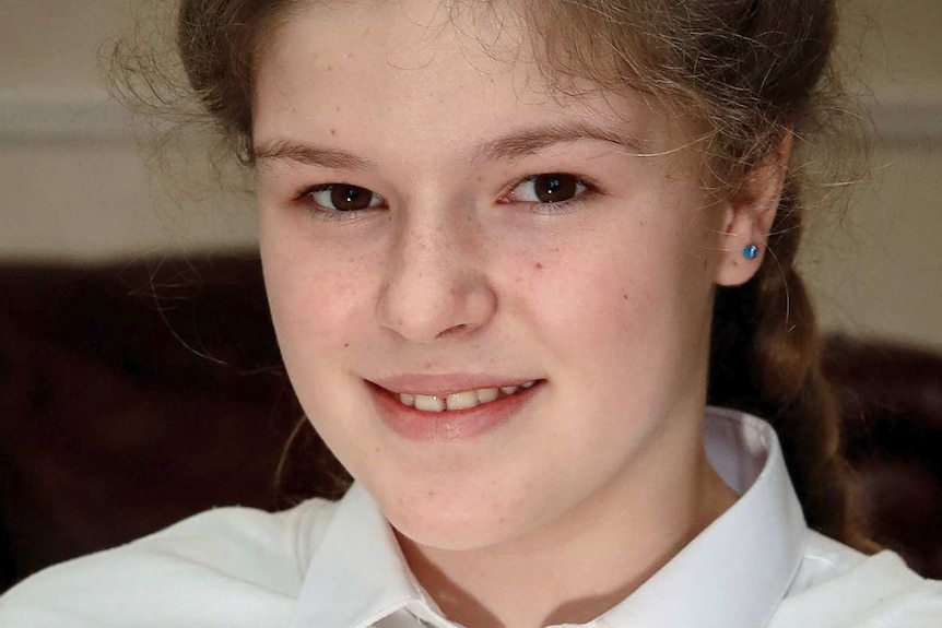 Close-up of 12-year-old Amelia Thompson smiling at the camera while wearing a jumper that says "one love Machester".