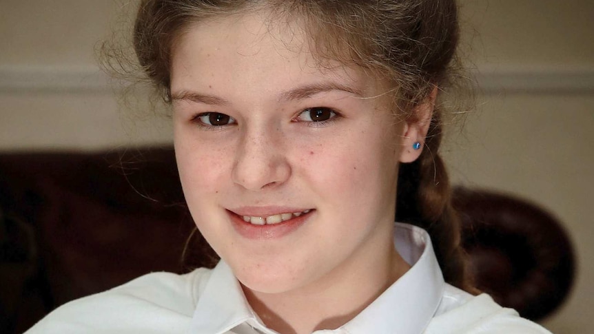 Close-up of 12-year-old Amelia Thompson smiling at the camera while wearing a jumper that says "one love Machester".