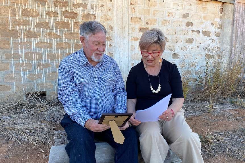 A man and a woman sitting on a log in front of a brick wall looking at photos. 