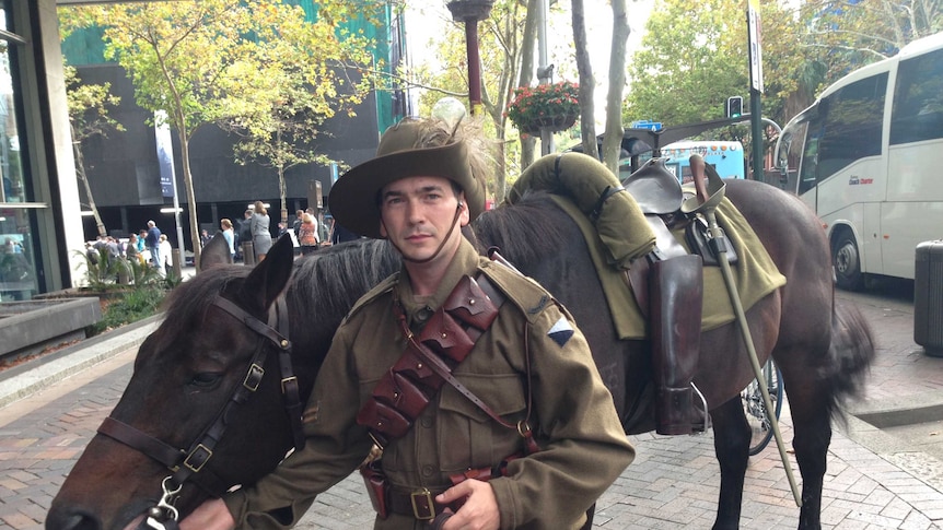 A man stands with a lone horse without a rider and boots backwards during the Sydney Anzac Day march