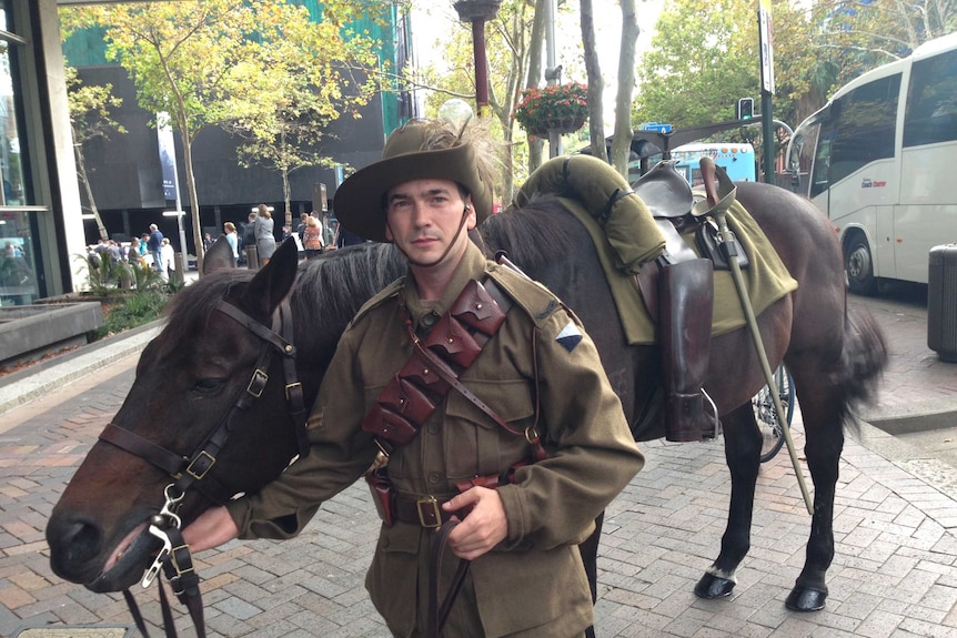 A man stands with a lone horse without a rider and boots backwards during the Sydney Anzac Day march