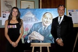 A young woman wearing war medals next to a man and an oil painting of Weary Dunlop.