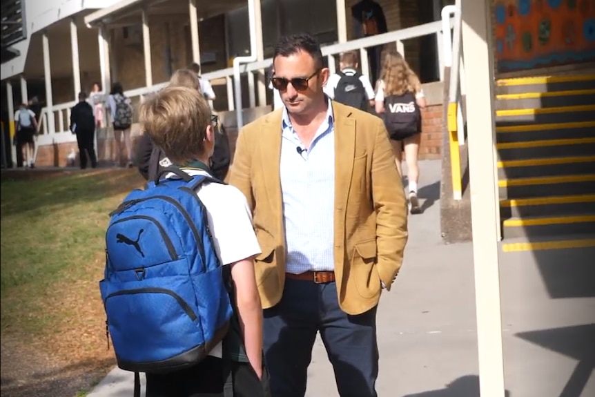 Student wearing blue backpack speaks to a teacher at kotara high school
