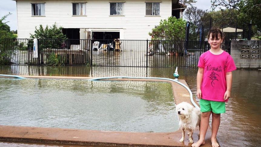Girl with her dog standing by her home's flooded pool and backyard north of Bundaberg.