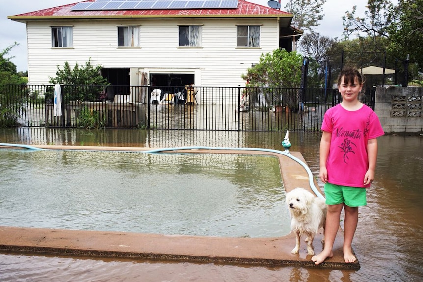 Girl with her dog standing by her home's flooded pool and backyard north of Bundaberg.