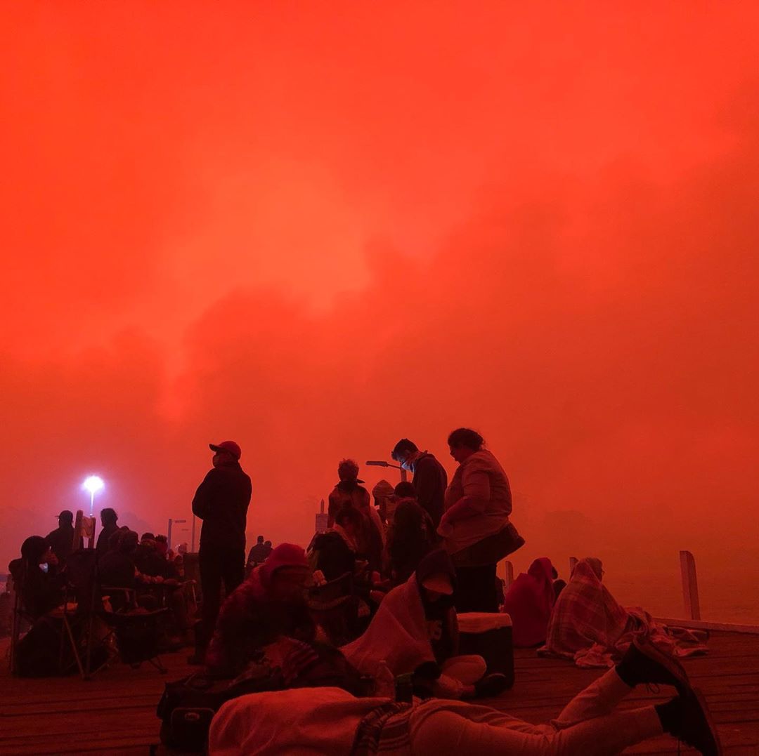 People seek refuge at Mallacoota Wharf under an orange sky.
