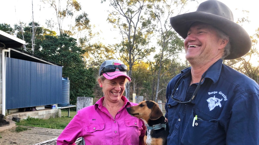 A husband and wife team share a laugh at the end of a long day of mustering, the man has the family's puppy under his arm