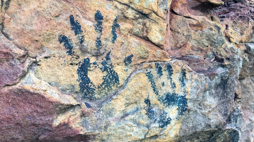 Two rock painting-style palm prints on a yellow and red rock formation.