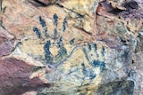 Two rock painting-style palm prints on a yellow and red rock formation.