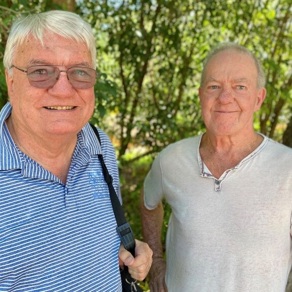 Mid shot of two men smiling at the camera, with trees in the background