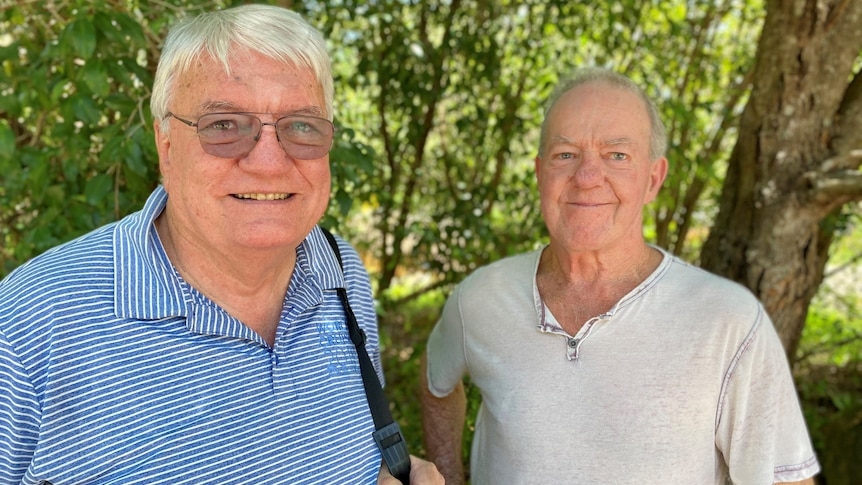 Mid shot of two men smiling at the camera, with trees in the background