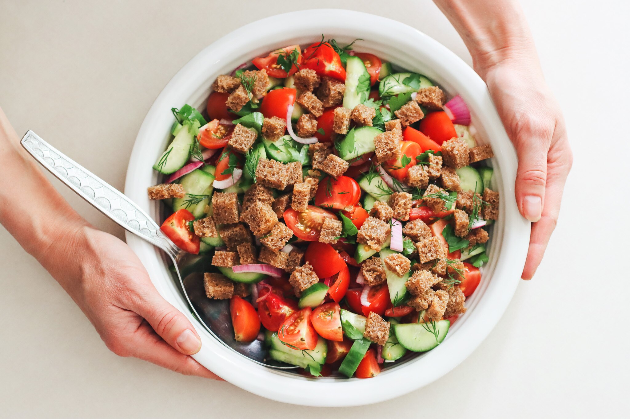 Un par de manos sostienen un cuenco lleno de ensalada de tomate y pepino.