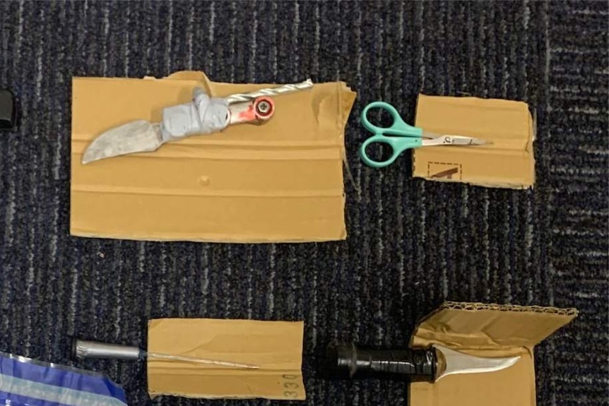 A meat cleaver, knife, pair of scissors, syringe and ice pick placed on top of cardboard