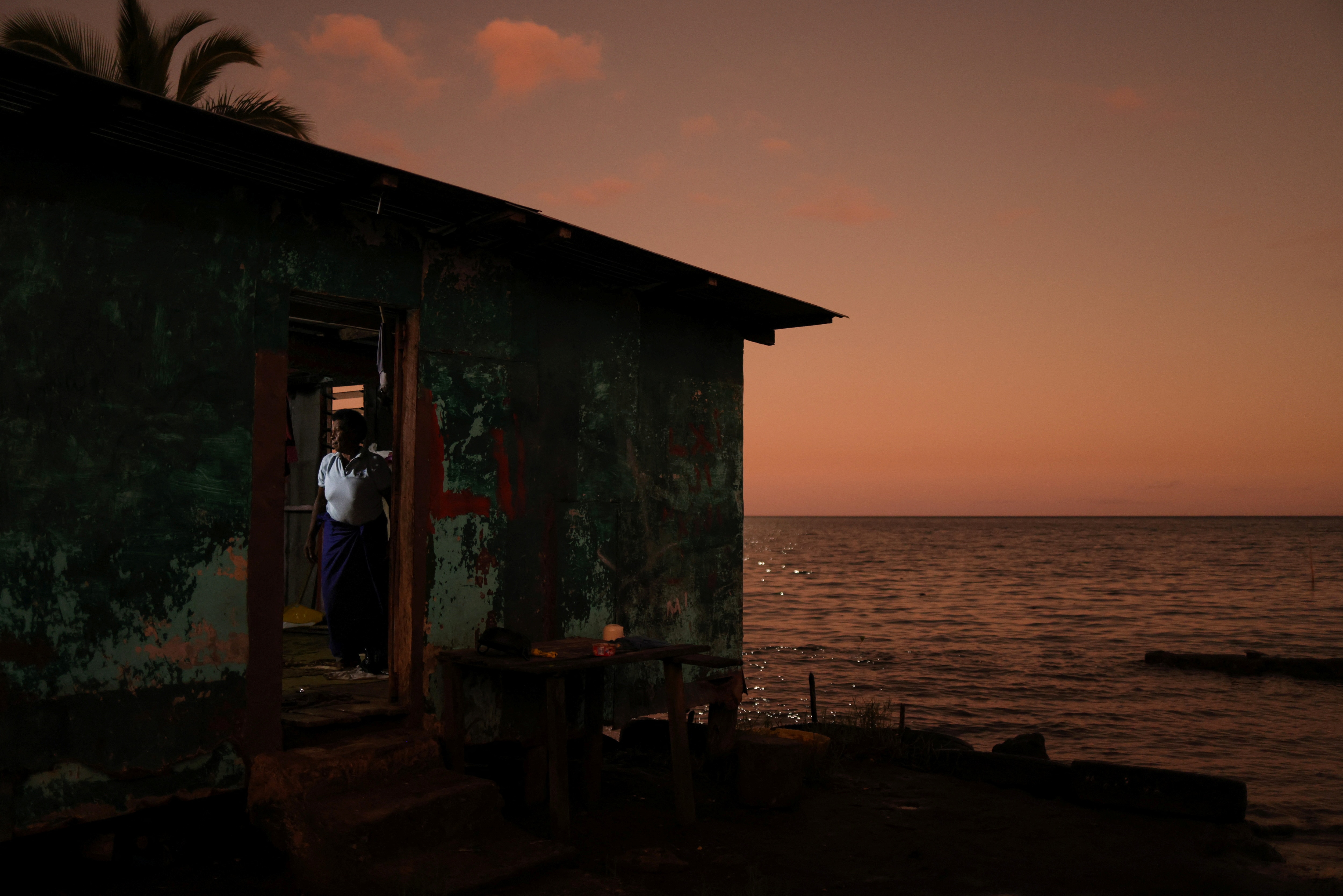 A woman in the door of her home, with seawater up to the threshold.