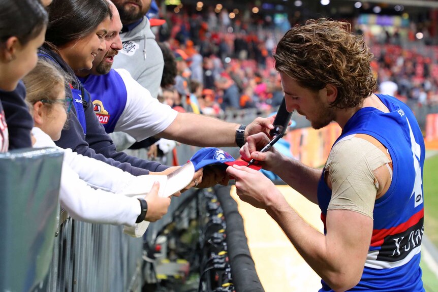 An AFL player gives his autograph to excited fans after a match.