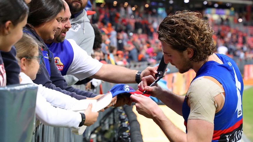 An AFL player gives his autograph to excited fans after a match.