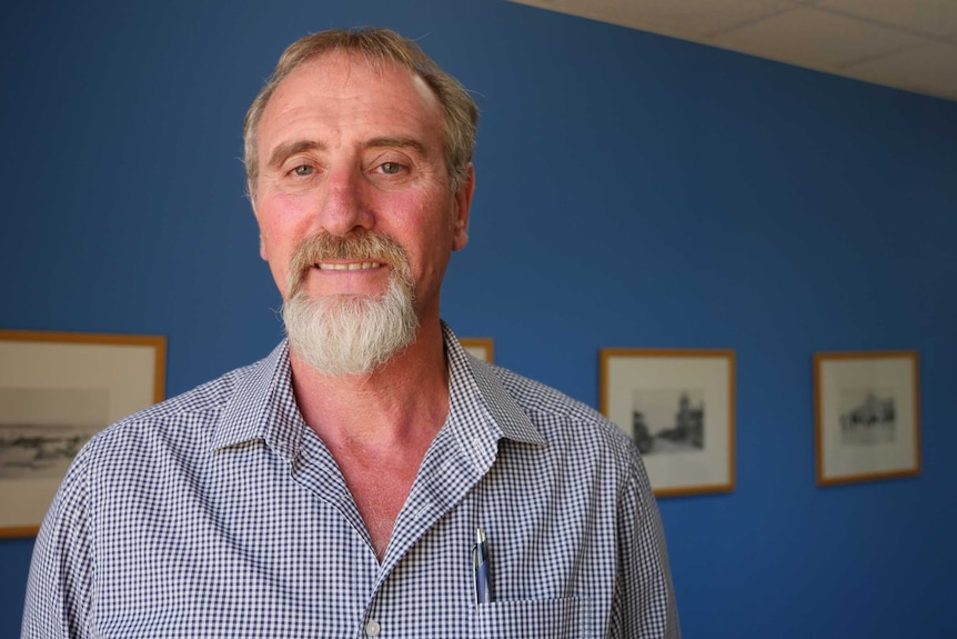 A bearded man smiles at the camera in a blue room.