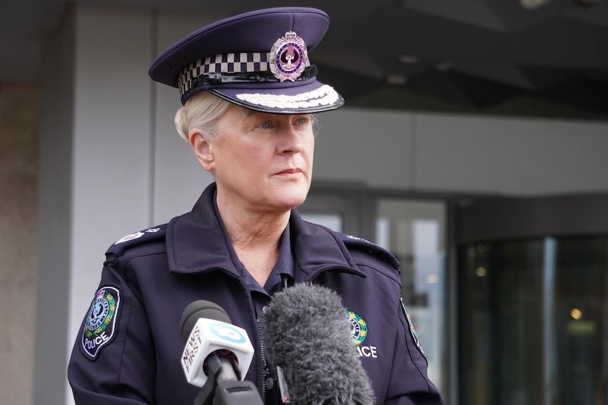 A female police officer in uniform speaking into microphone in front of a building