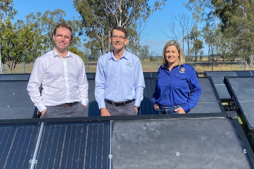 Two men and a woman, all in blue shirts, standing between large hydropanels on the ground.