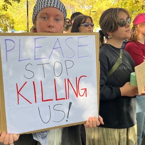 Woman holds a sign saying 'Please Stop Killing Us!'