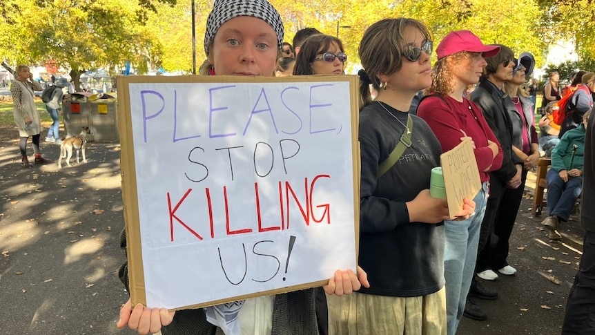 Woman holds a sign saying 'Please Stop Killing Us!'
