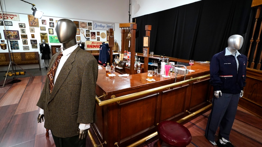 Mannequins in suits from Cheers show are on display next to bar used in US sitcom.