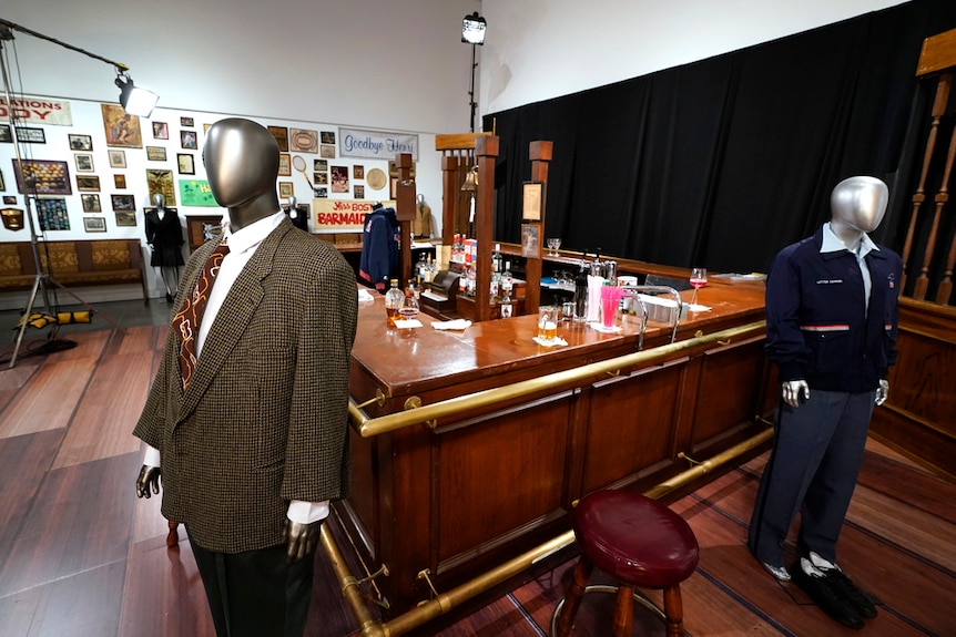 Mannequins in suits from 'Cheers' show are on display next to bar used in US sitcom.