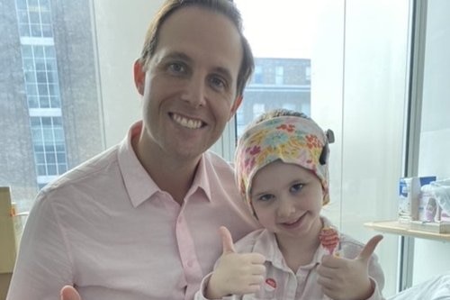 Middle aged man with pink shirt with a small child wearing a surgical cap.