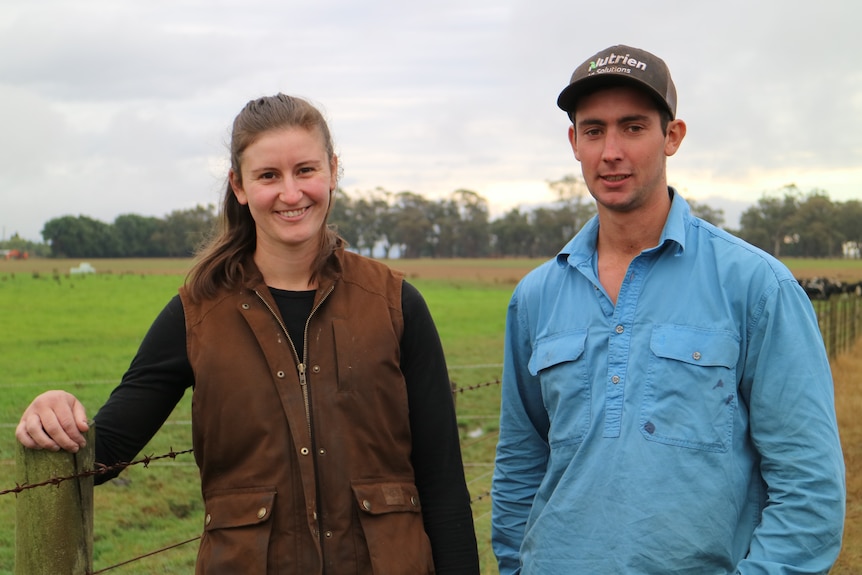 a young man and woman stand in front of a barbed wire fence on a farm