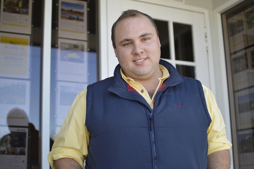 A man standing in front of a real estate agency.