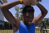 A sprinter holds both hands above his head and looks tired after running