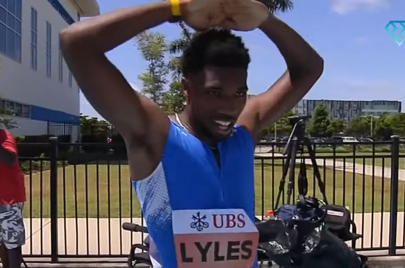 A sprinter holds both hands above his head and looks tired after running