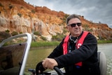 Tony Sharley drives a small boat down the river with cliffs in the background
