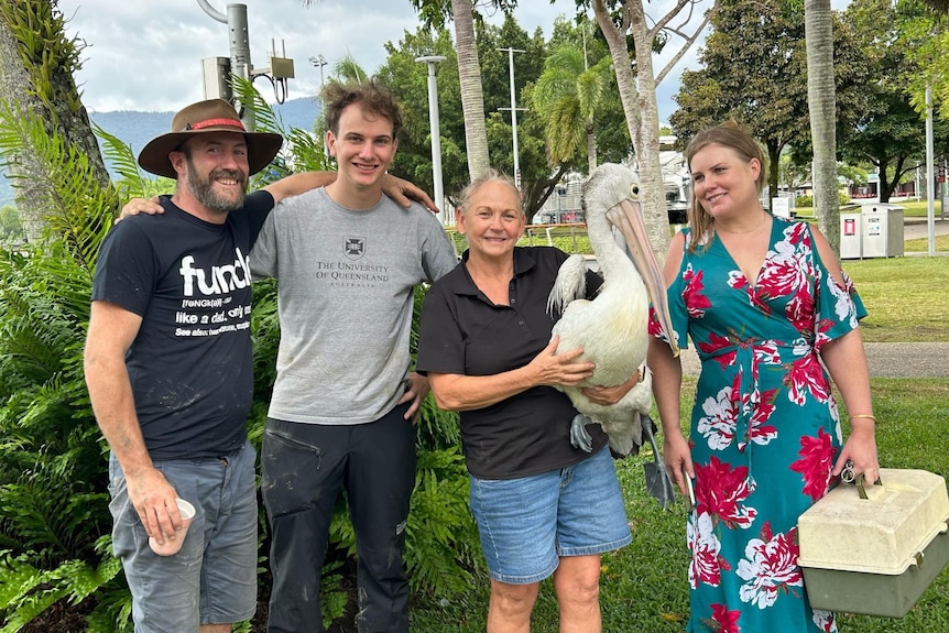 Two men and two women, one holding a pelican, stand smiling in a beachside park.