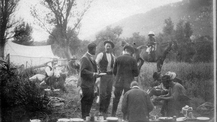 A group of men stand around a campsite in the bush in 1905