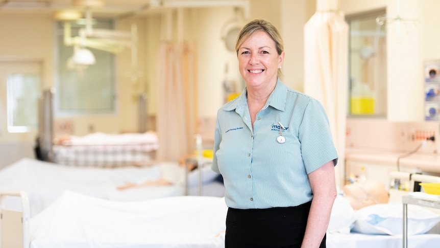 Louise Dingle in a nurse uniform smiling, beds and patients behind her.