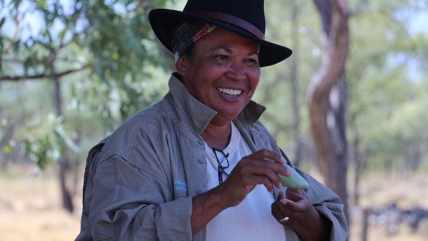 Woman in the outback heat smiling while holding bush food 