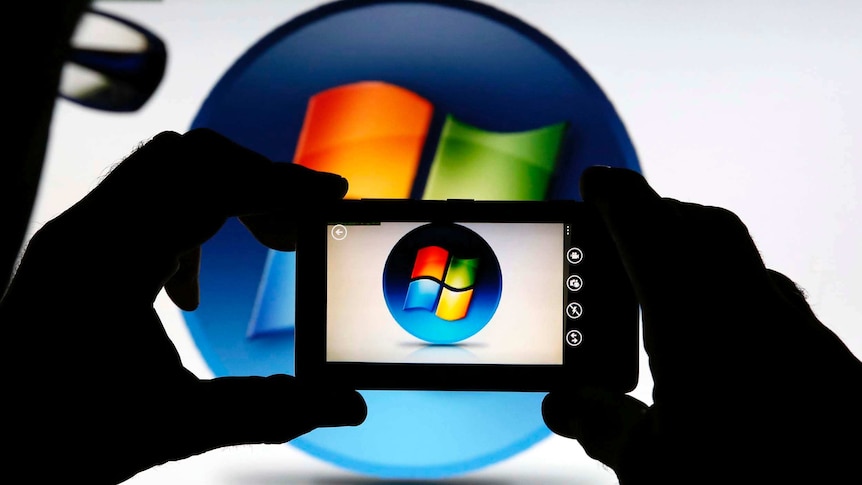 A man uses a mobile phone to take a photo of Microsoft Windows logo.