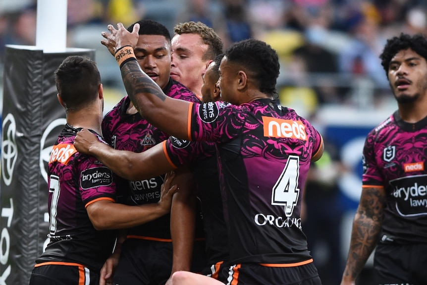 Teammates pat an NRL player next to the posts to congratulate him after a try.