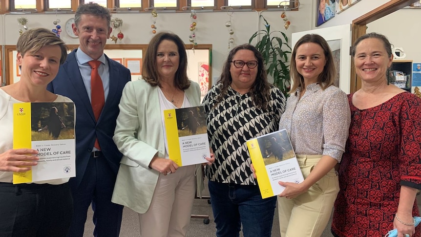 Six people stand together holding a copy of the report